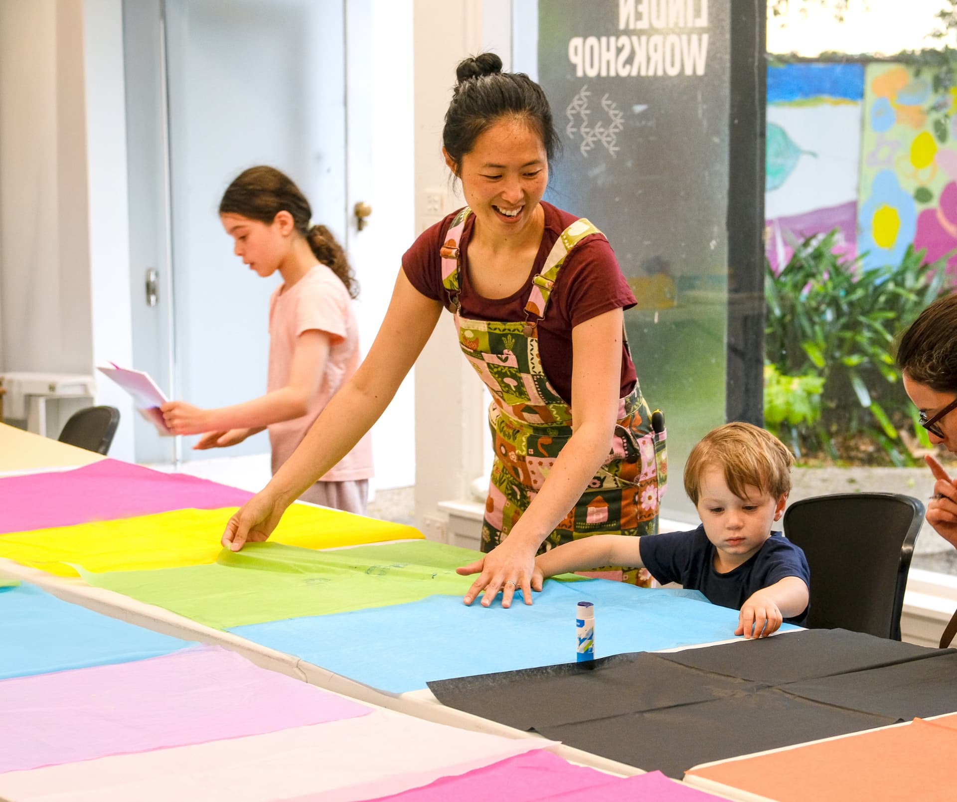 Jen Tran smiling as she leads a tissue-paper collage workshop with children at the Linden Workshop